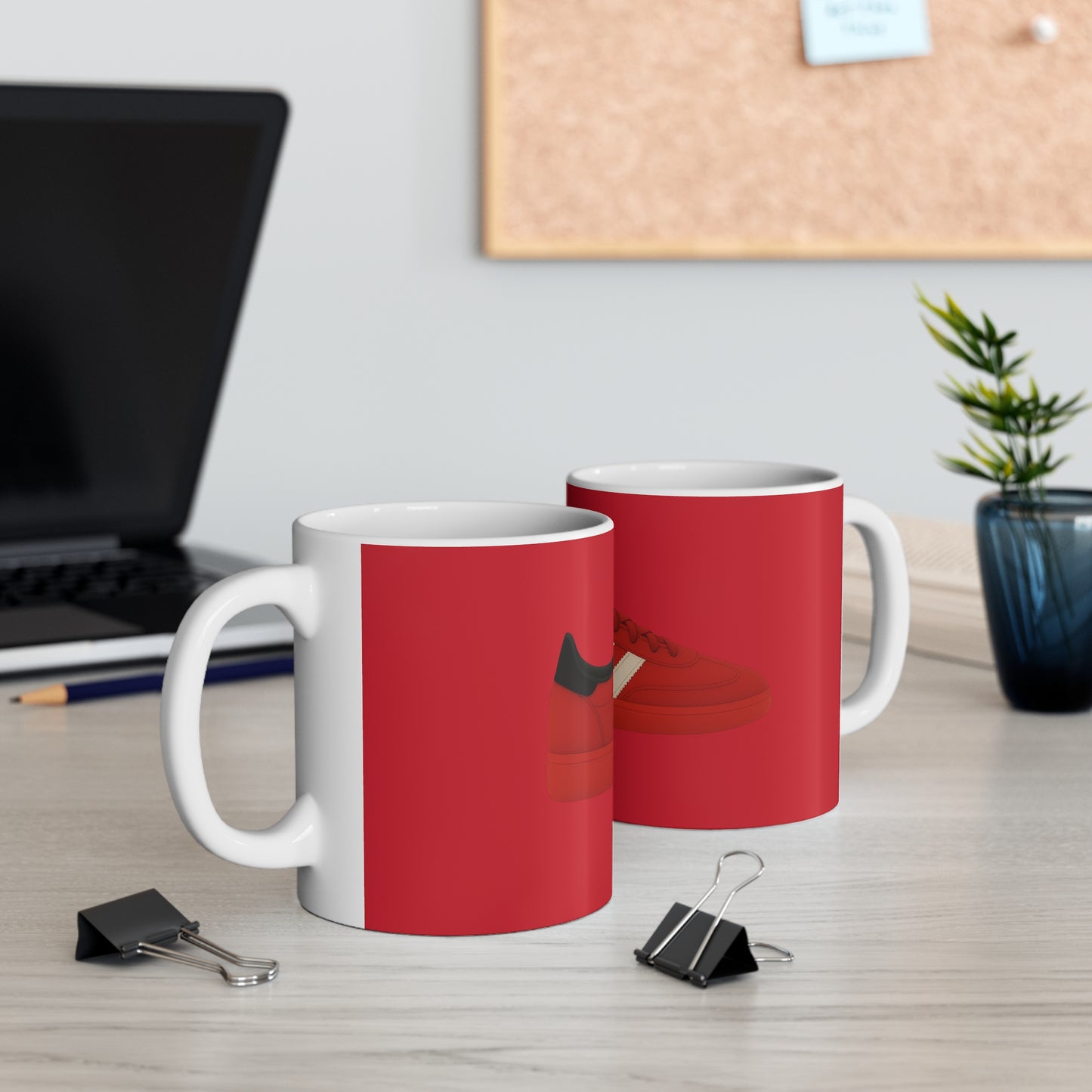 White ceramic mugs with red sneaker design on a office desk with laptop and plant