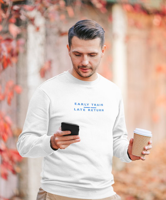 Man checking his phone on an autumn street wearing the white Early Train, Late Return sweatshirt