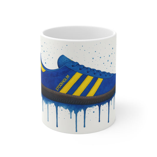White coffee mug featuring blue and yellow Adidas Stockholm sneaker graphic with paint drip effect