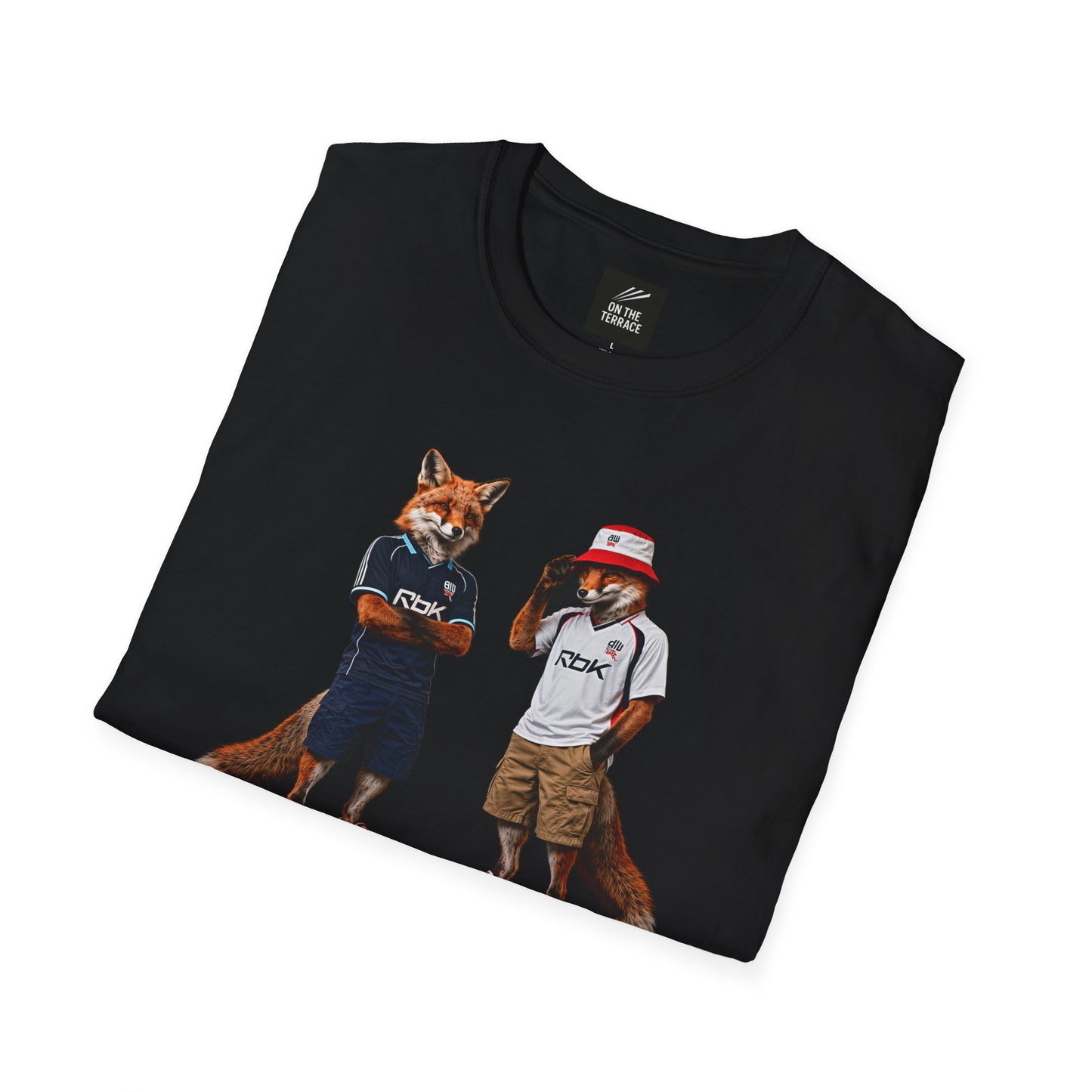 A black graphic t-shirt laid flat, featuring a central design by On The Terrace for Bolton fans. The graphic showcases two anthropomorphic English foxes dressed in vintage Rbk Bolton-inspired football kits. The fox on the left wears the dark blue retro away jersey with arms crossed, while the fox on the right sports the classic white home shirt, a red and white bucket hat, and cargo shorts. The inner neck of the tee features the official "On The Terrace" brand logo