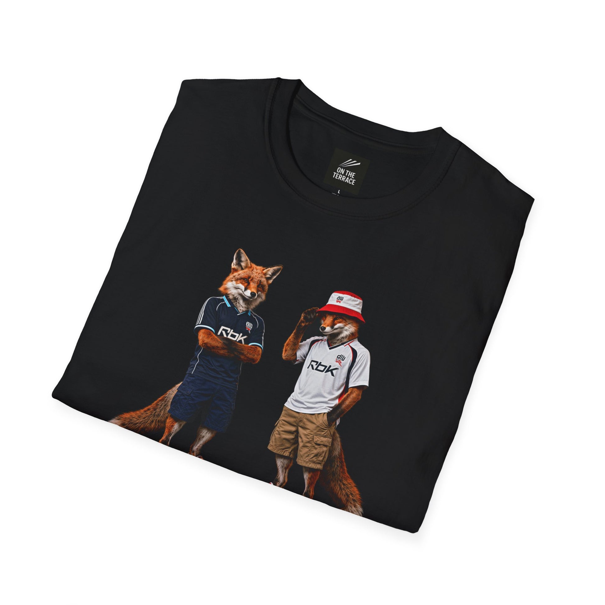 A black graphic t-shirt laid flat, featuring a central design by On The Terrace for Bolton fans. The graphic showcases two anthropomorphic English foxes dressed in vintage Rbk Bolton-inspired football kits. The fox on the left wears the dark blue retro away jersey with arms crossed, while the fox on the right sports the classic white home shirt, a red and white bucket hat, and cargo shorts. The inner neck of the tee features the official "On The Terrace" brand logo
