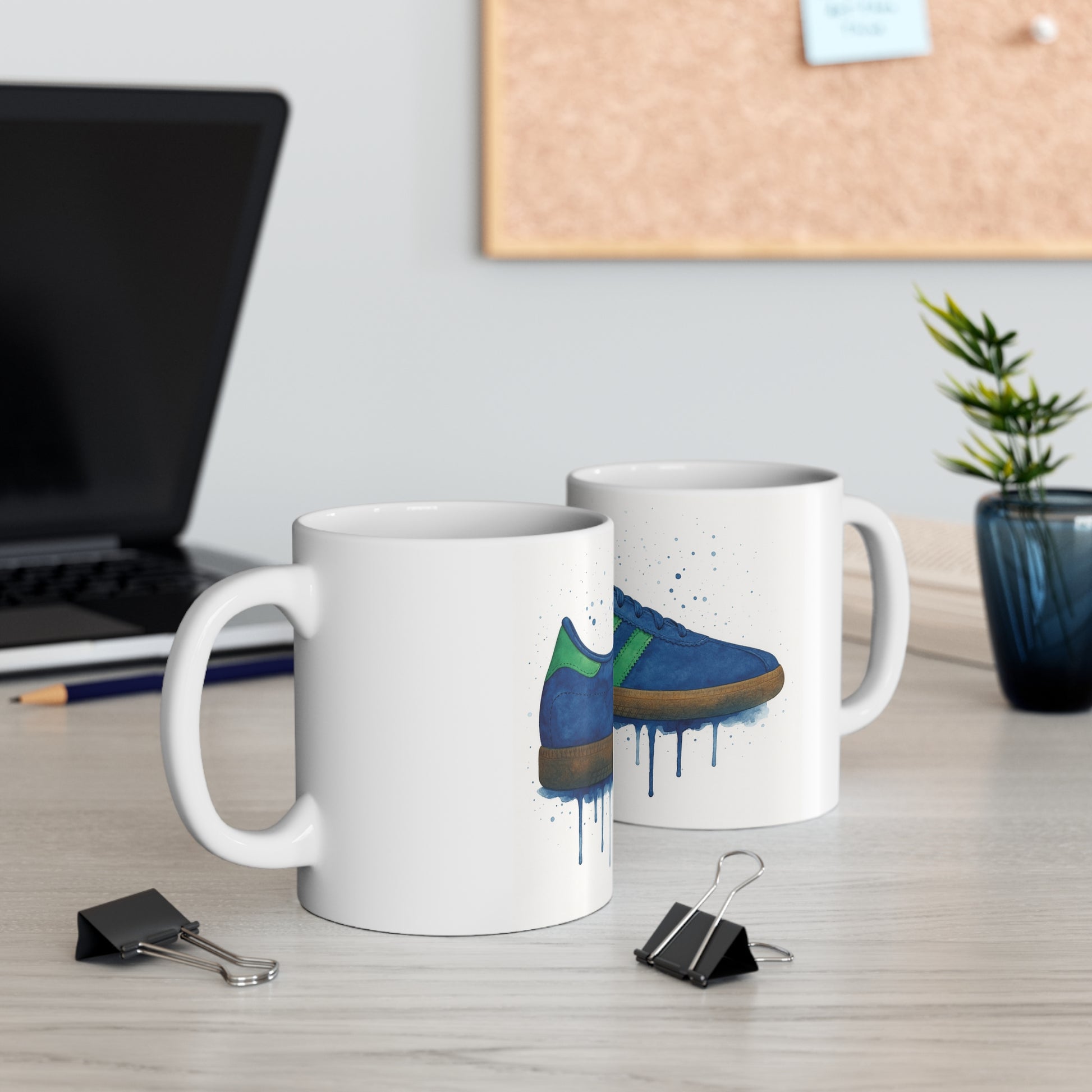 Two white mugs on desk featuring blue and green sneaker print with paint drip effect, office setting