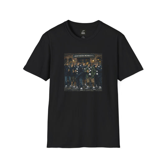 A black, short-sleeved crewneck t-shirt featuring a large, colorful rectangular graphic on the chest. The artwork depicts a group of seven chimpanzees standing in front of a traditional brick pub with a sign that reads "THE NORTHERN MONKEY'S". The monkeys are dressed in classic British "terrace culture" or "football casual" fashion, wearing olive and navy parkas, puffer jackets, black-and-white striped scarves, and black  trainers with white stripes. Some of the figures are shown holding bottles.