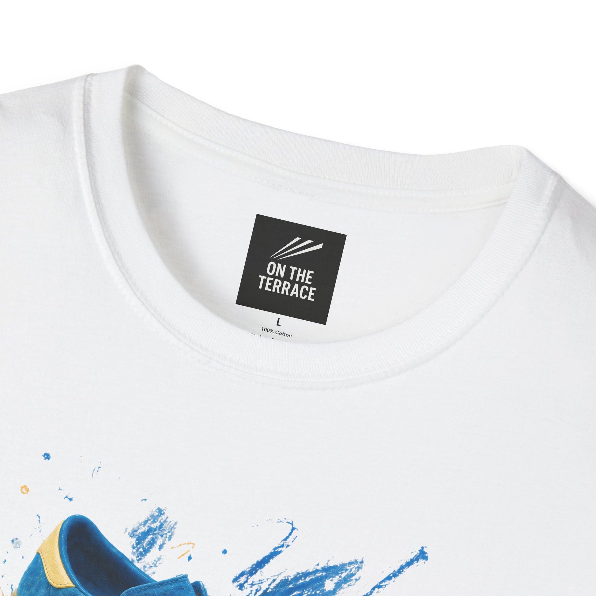 White t-shirt with a graphic print of a blue suede trainer with cream three stripes and gum sole, set against a blue and gold paint-splash background, On The Terrace neck label visible.