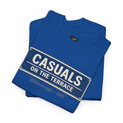 A folded a royal blue heavy cotton  SWFC t-shirt flat lay featuring a central vintage blue and white street sign graphic reading "CASUALS ON THE TERRACE" with "Hillsborough • 1867" printed below, and an inner neck label for On The Terrace' in white and gray, set against a plain white background.