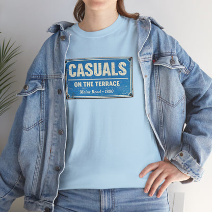 A person wearing a light blue MCFC t-shirt with a vintage-style blue and white sign graphic that reads 'CASUALS ON THE TERRACE Maine Road + 1880', layered under an oversized light-wash denim jacket.