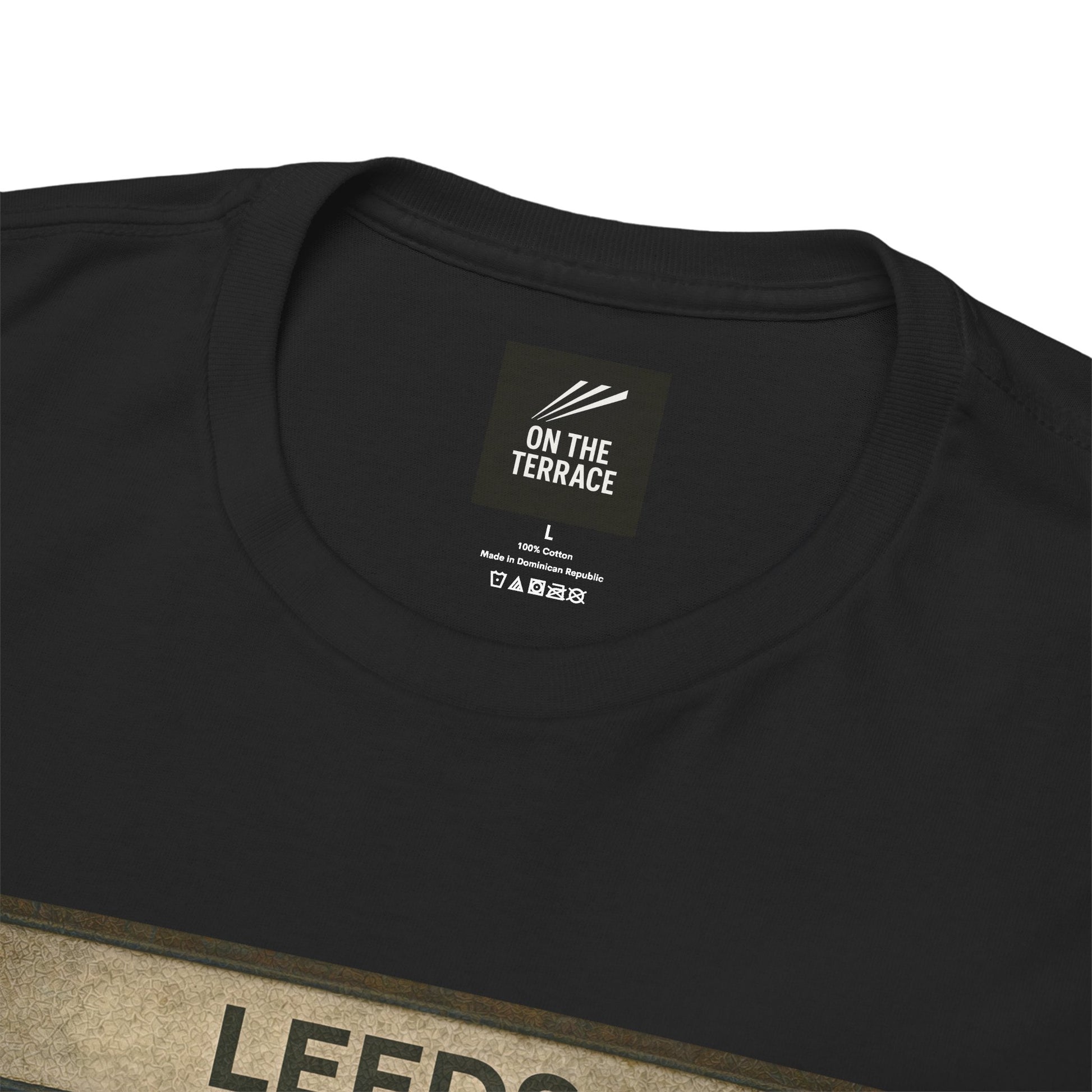 Close-up of a black crewneck Leeds t-shirt showing the inner neck label which reads 'ON THE TERRACE' and a portion of a beige graphic print at the bottom.