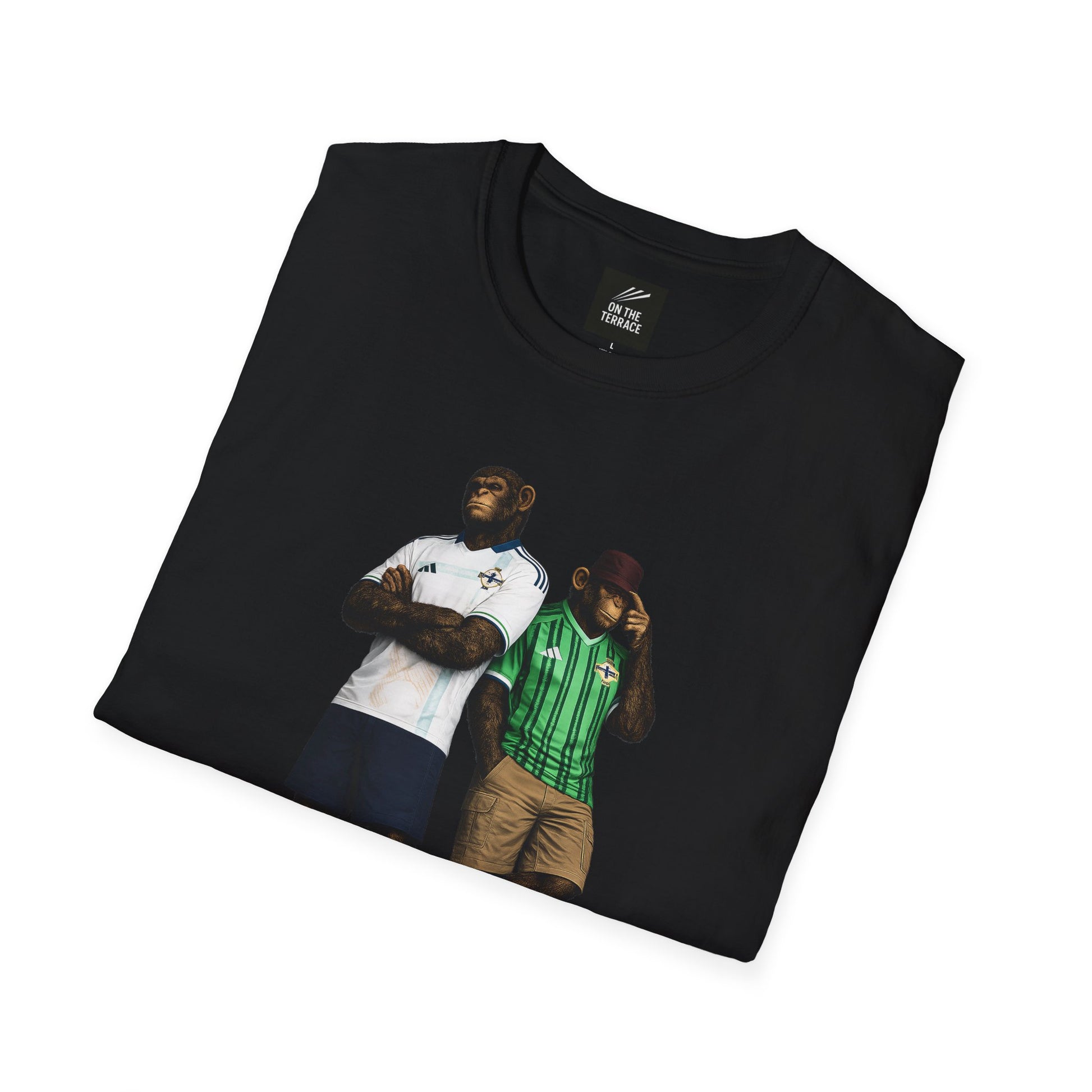 Folded black short-sleeved t-shirt featuring a central graphic of two chimpanzees styled as Northern Ireland national team supporters. The chimpanzee on the left stands with arms crossed, wearing a white away jersey with blue trim and the Northern Ireland crest. The chimpanzee on the right wears the classic green home jersey with vertical stripes, khaki cargo shorts, and a maroon bucket hat