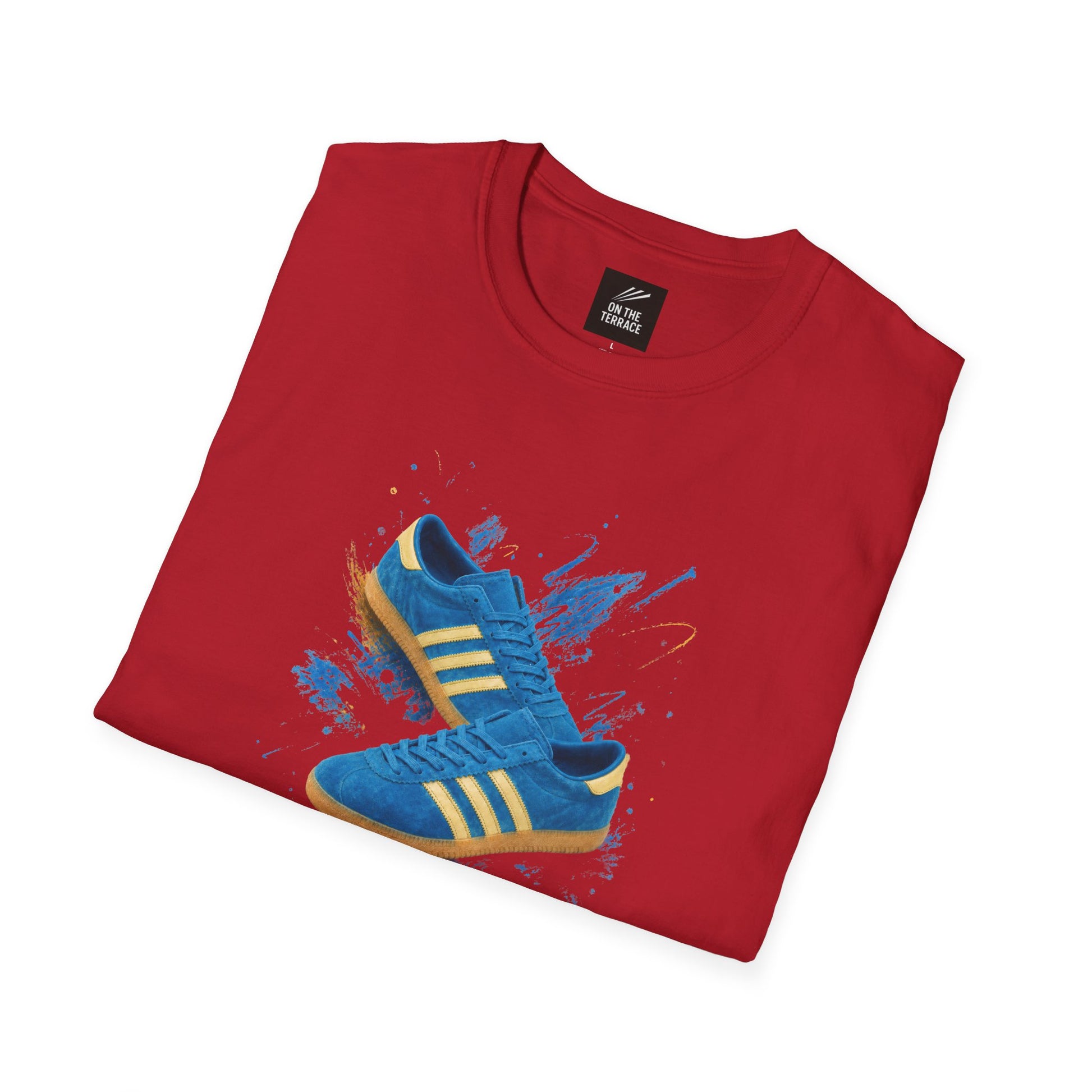 A folded red t-shirt with a graphic print of blue Adidas sneakers on a paint splatter background, displayed on a clean white background.