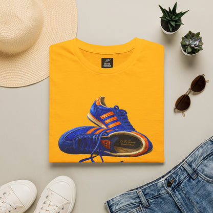 A folded yellow t-shirt with hand-illustrated blue and orange retro terrace trainer sneaker graphic print, On The Terrace casual clothing brand
