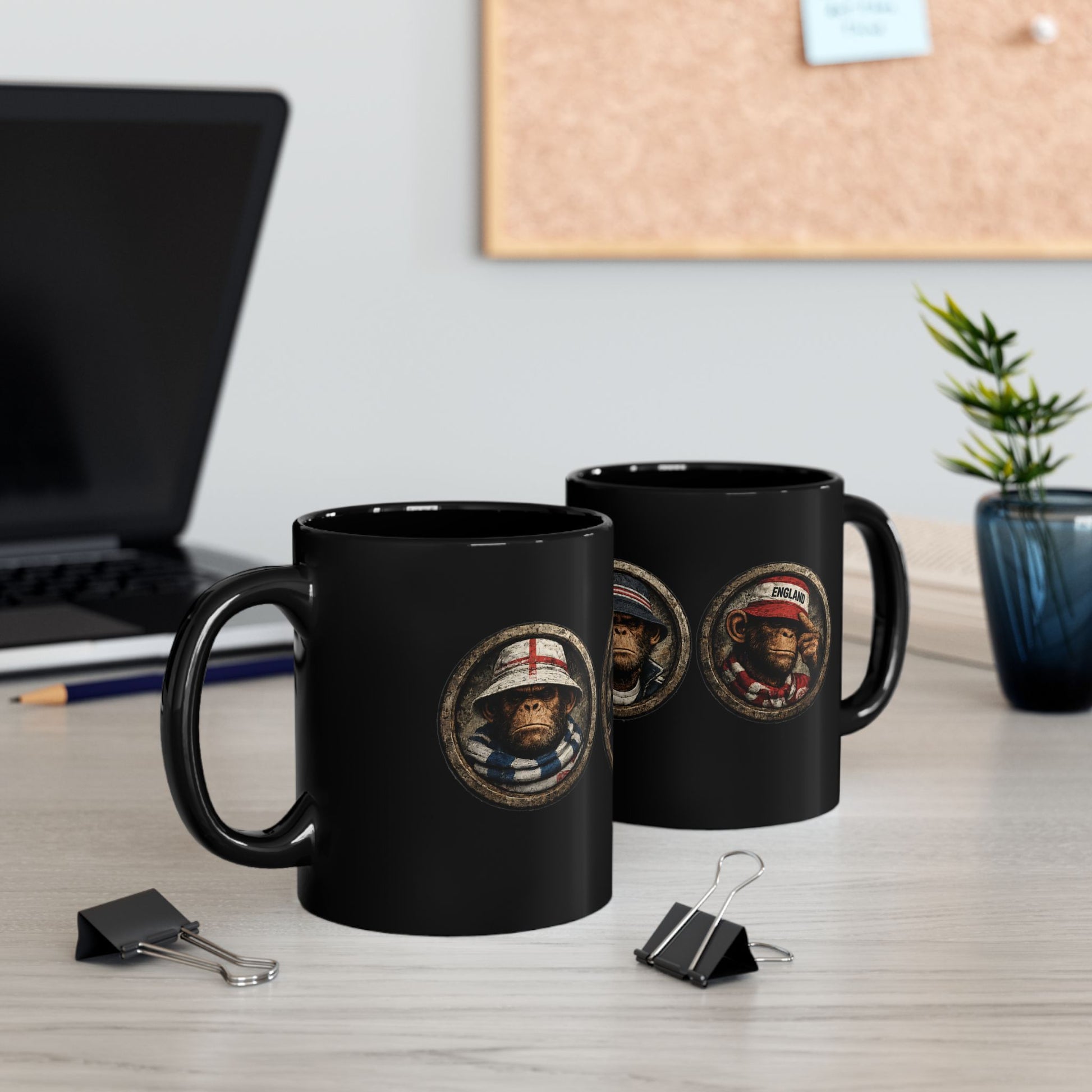 A black ceramic mug features three circular, stone-textured portrait emblems. The central emblem showcases a chimpanzee with a stern expression, wearing a navy blue casual jacket and a navy bucket hat with red and white stripes. The left emblem shows a monkey wearing an England St. George's cross bucket hat and a blue-and-white bar scarf. The right emblem shows a monkey in a red casual cap and scarf.