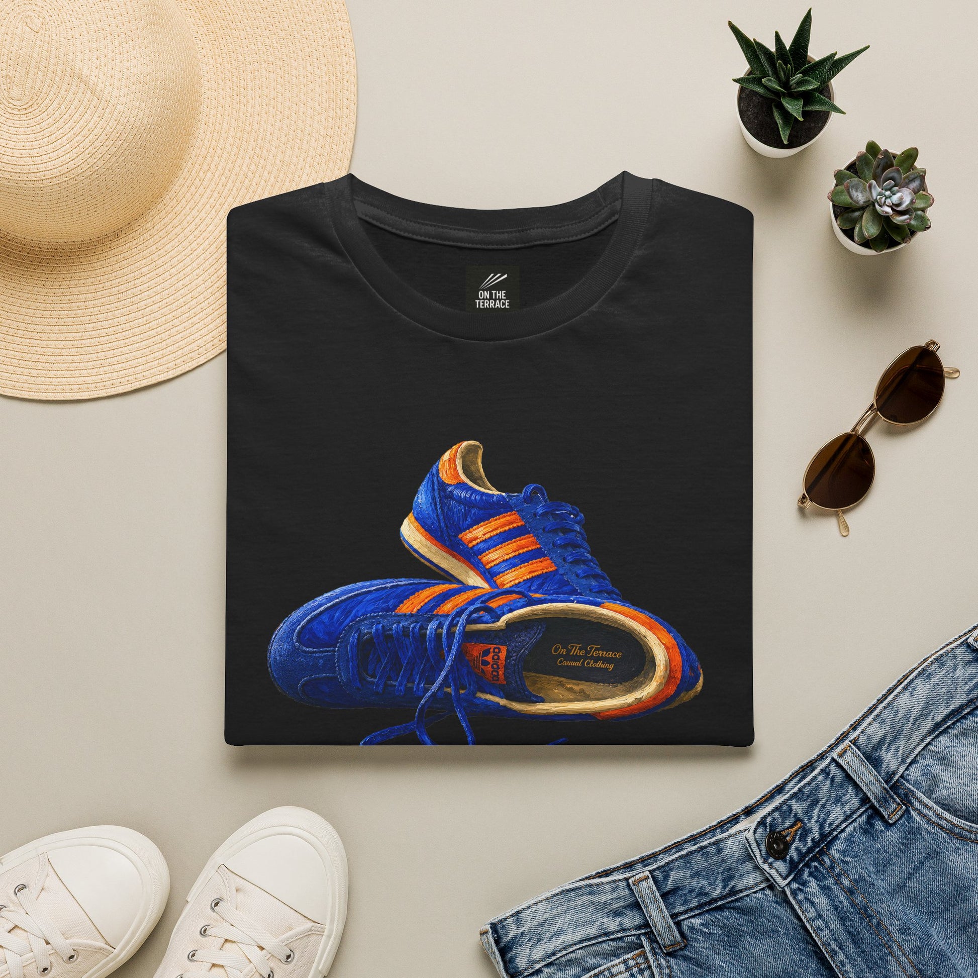 A black folded t-shirt with hand-illustrated blue and orange retro terrace trainer sneaker graphic print, On The Terrace casual clothing brand
