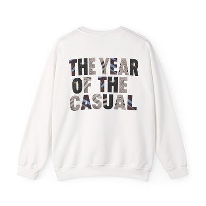 A white crewneck sweatshirt shown from the back, featuring the text 'THE YEAR OF THE CASUAL' printed in a bold, multi-colored camouflage pattern.