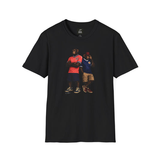 A black short-sleeved t-shirt featuring a central graphic of two chimpanzees styled as Scotland national football team fans. The chimpanzee on the left stands with arms crossed, wearing the iconic 1986 pink and yellow striped away jersey with navy shorts. The chimpanzee on the right wears a classic navy blue Scotland home jersey with white trim, khaki cargo shorts, and a maroon bucket hat on a white background