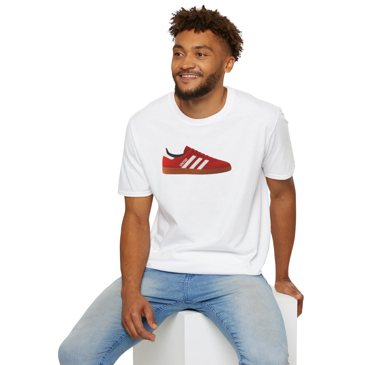 Man wearing white t-shirt with red sneaker graphic and light blue jeans sitting on white cube