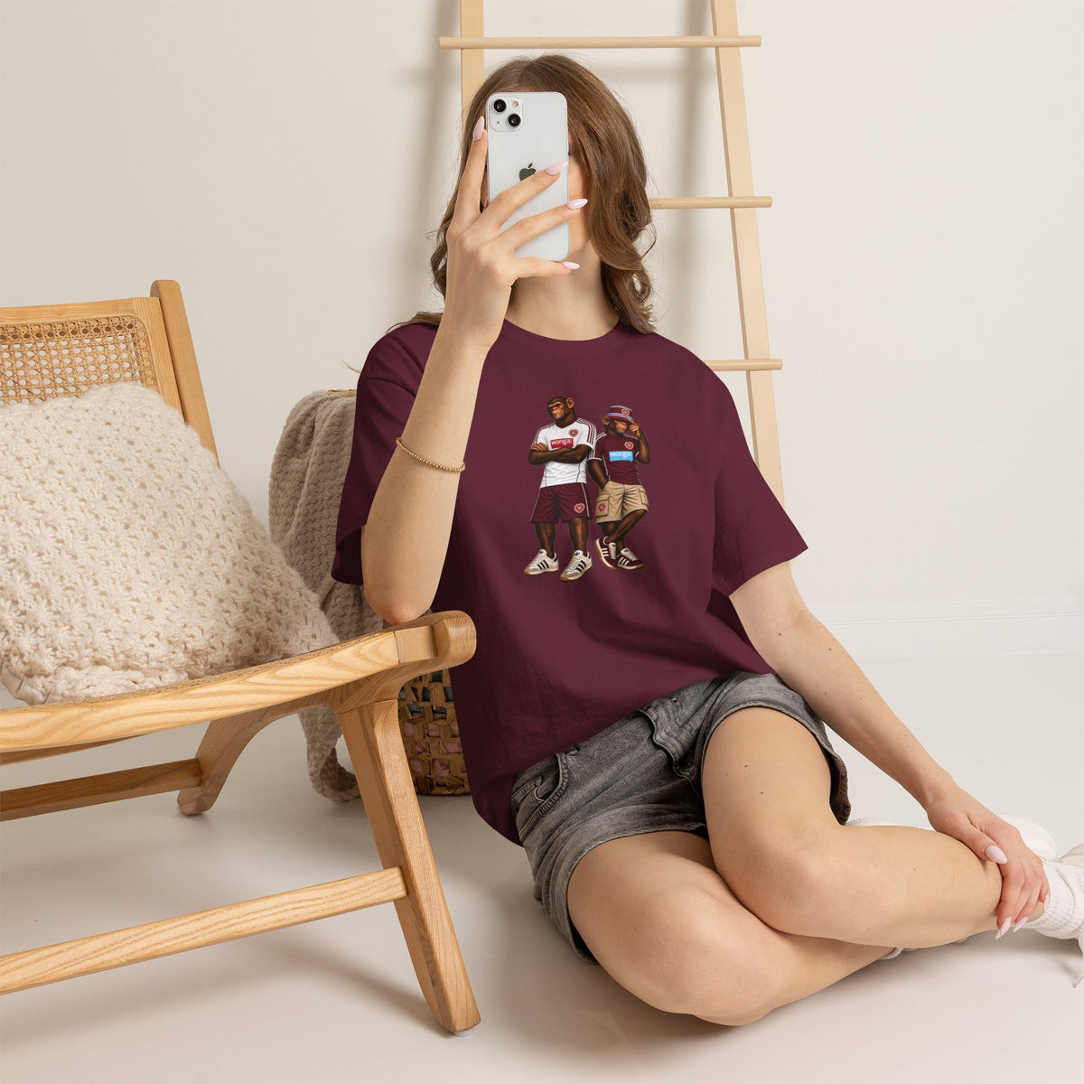 Woman in a chair taking a selfie in the maroon Hearts Monkeys Duo tee
