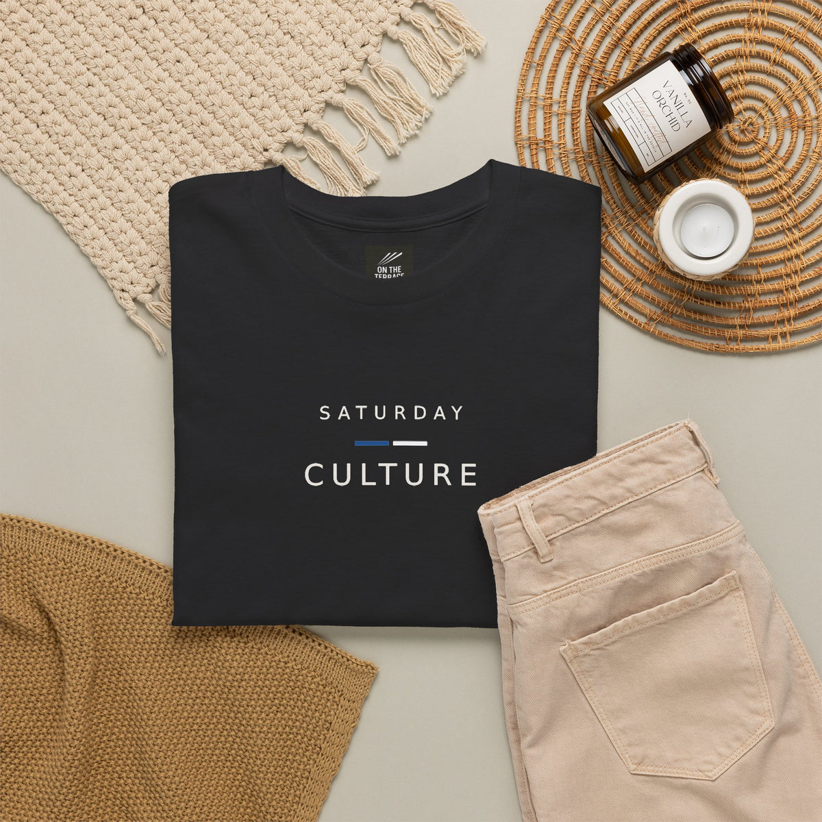 Black Saturday Culture tee flat lay with knitwear, cord trousers and candle