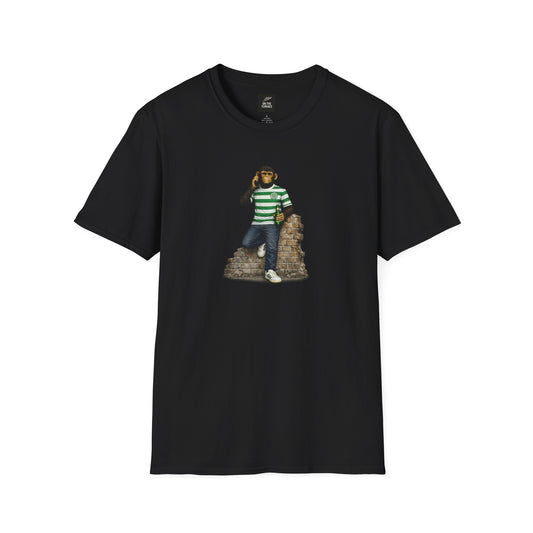 A black short-sleeved t-shirt featuring a central graphic of a chimpanzee wearing a green and white hooped football jersey, denim jeans, and white trainers. He is leaning against a section of a ruined brick wall while holding a green bottle and talking on a mobile phone.