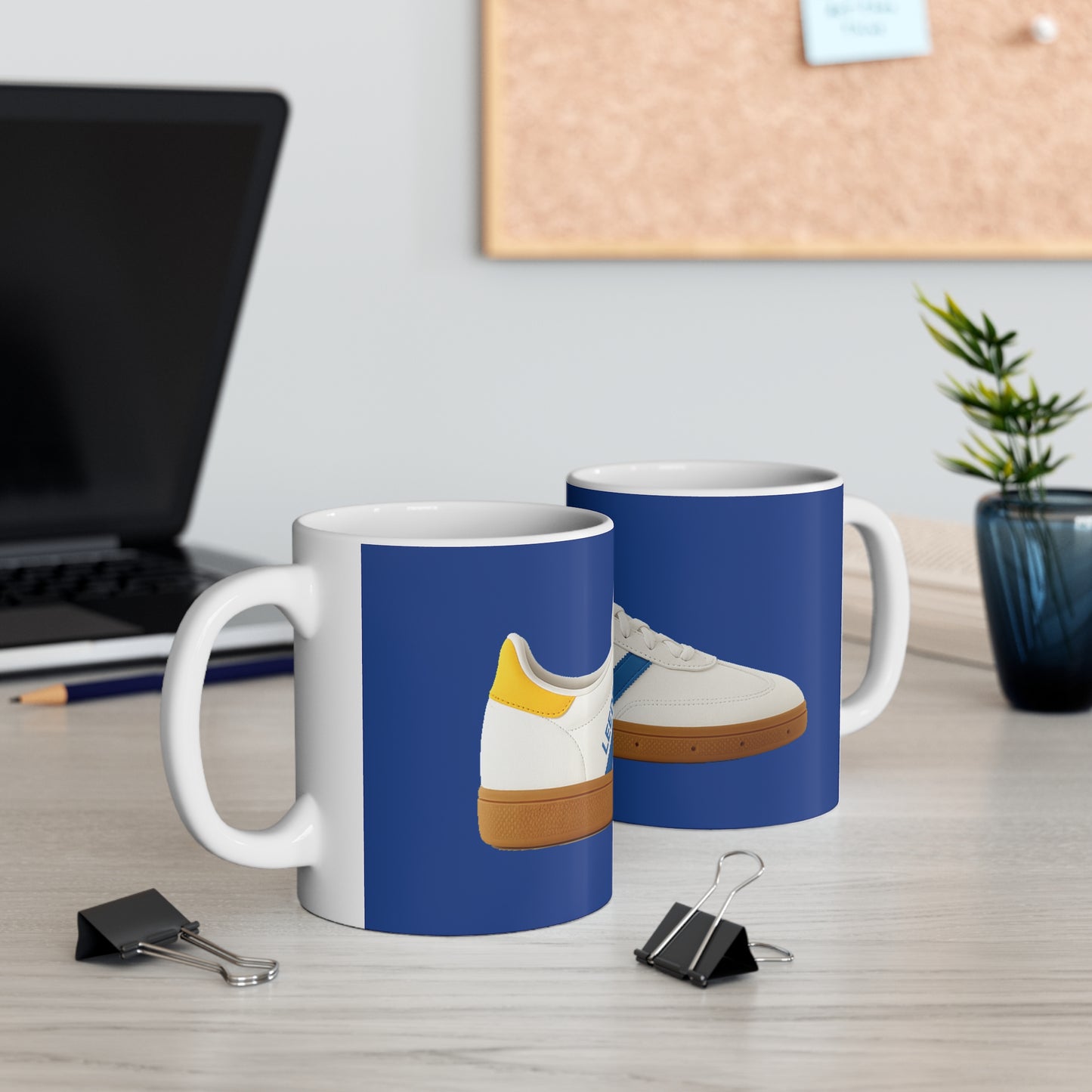 White mugs with blue background featuring white sneakers with yellow and blue accents on office desk