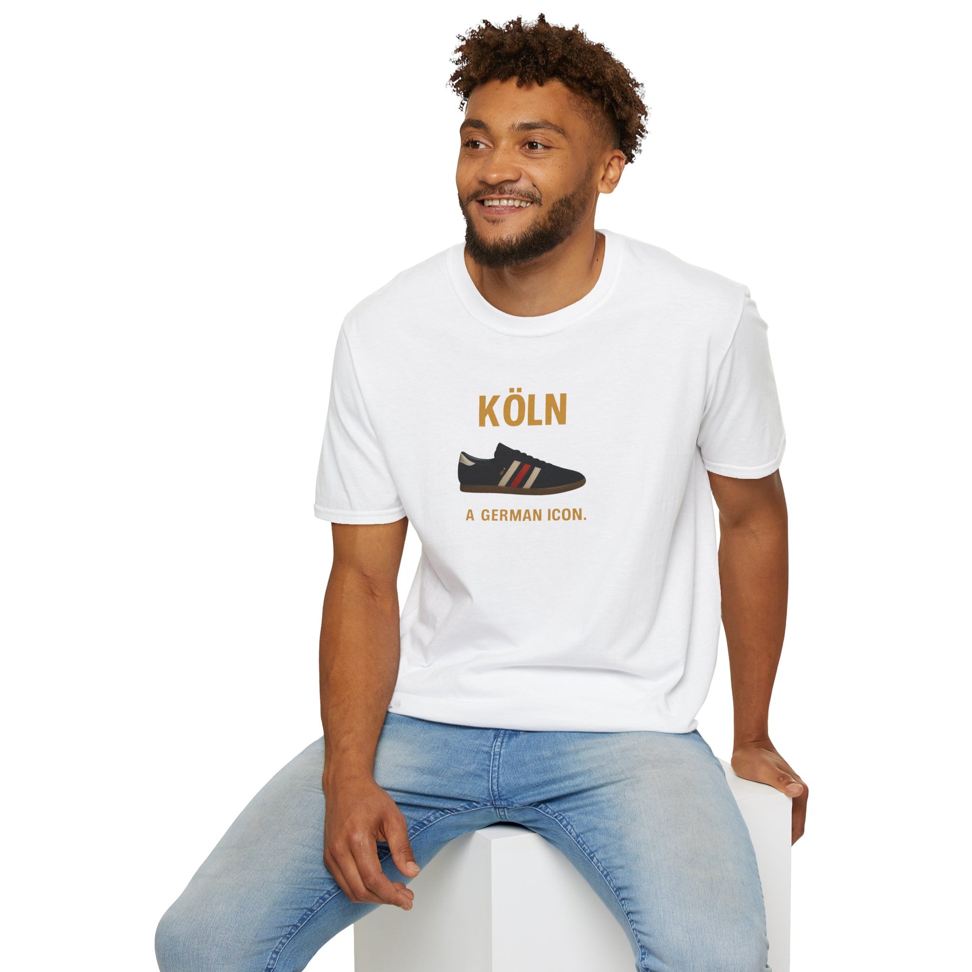 Smiling man wearing white t-shirt with Köln sneaker design and blue jeans seated on white block