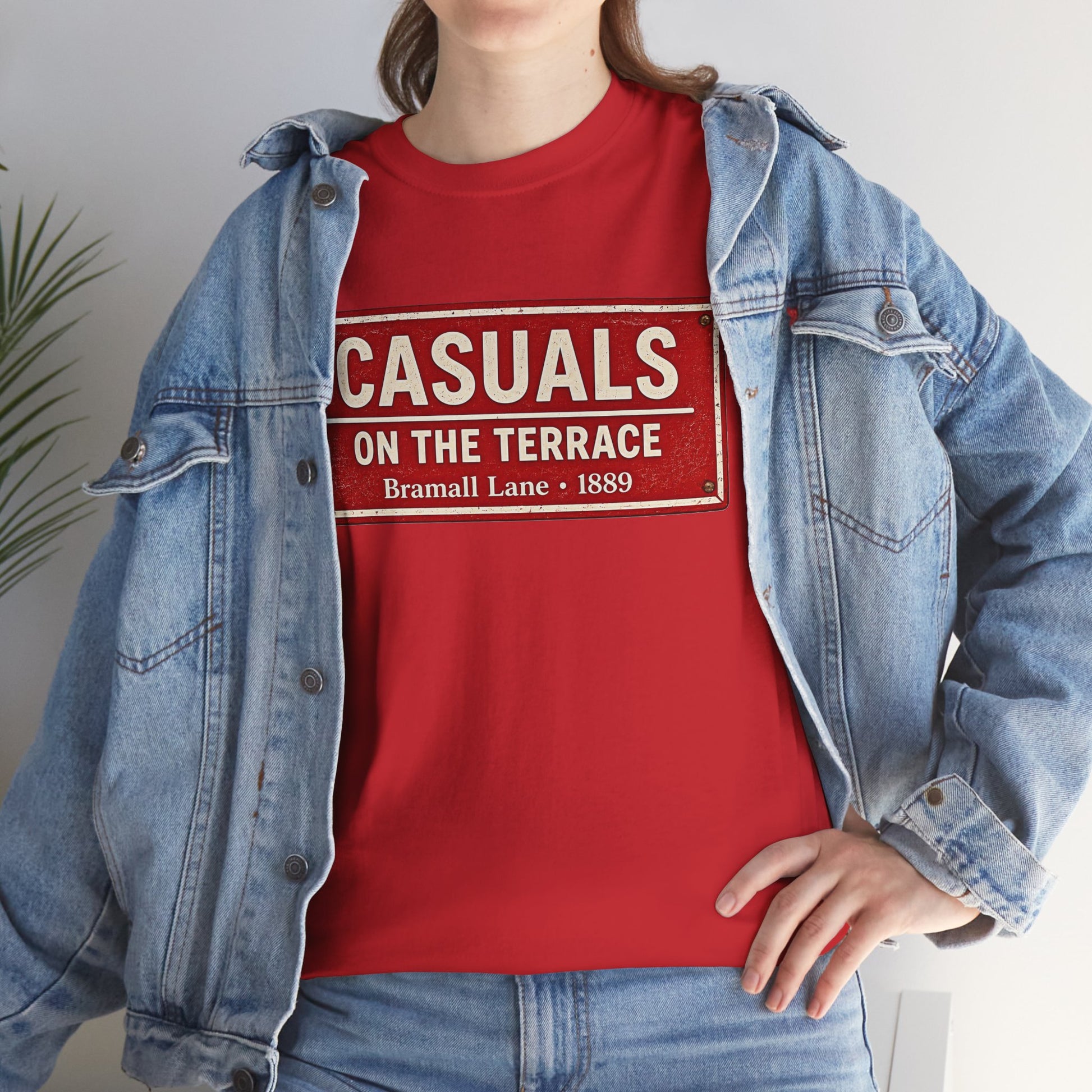 A person wearing a red SUFC T-shirt under an open light-wash denim jacket, with the shirt reading 'CASUALS ON THE TERRACE Bramall Lane 1889'.