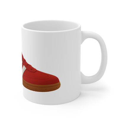 A white ceramic coffee mug featuring a graphic print from the file from On The Terrace, showing a classic red retro terrace trainer with three white stripes, a brown gum sole, and the word "GUNNERS" printed on the side.