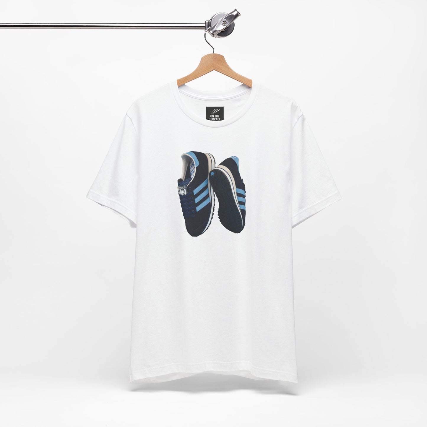 White t-shirt hanging on wooden hanger with printed design of black and blue sneakers
