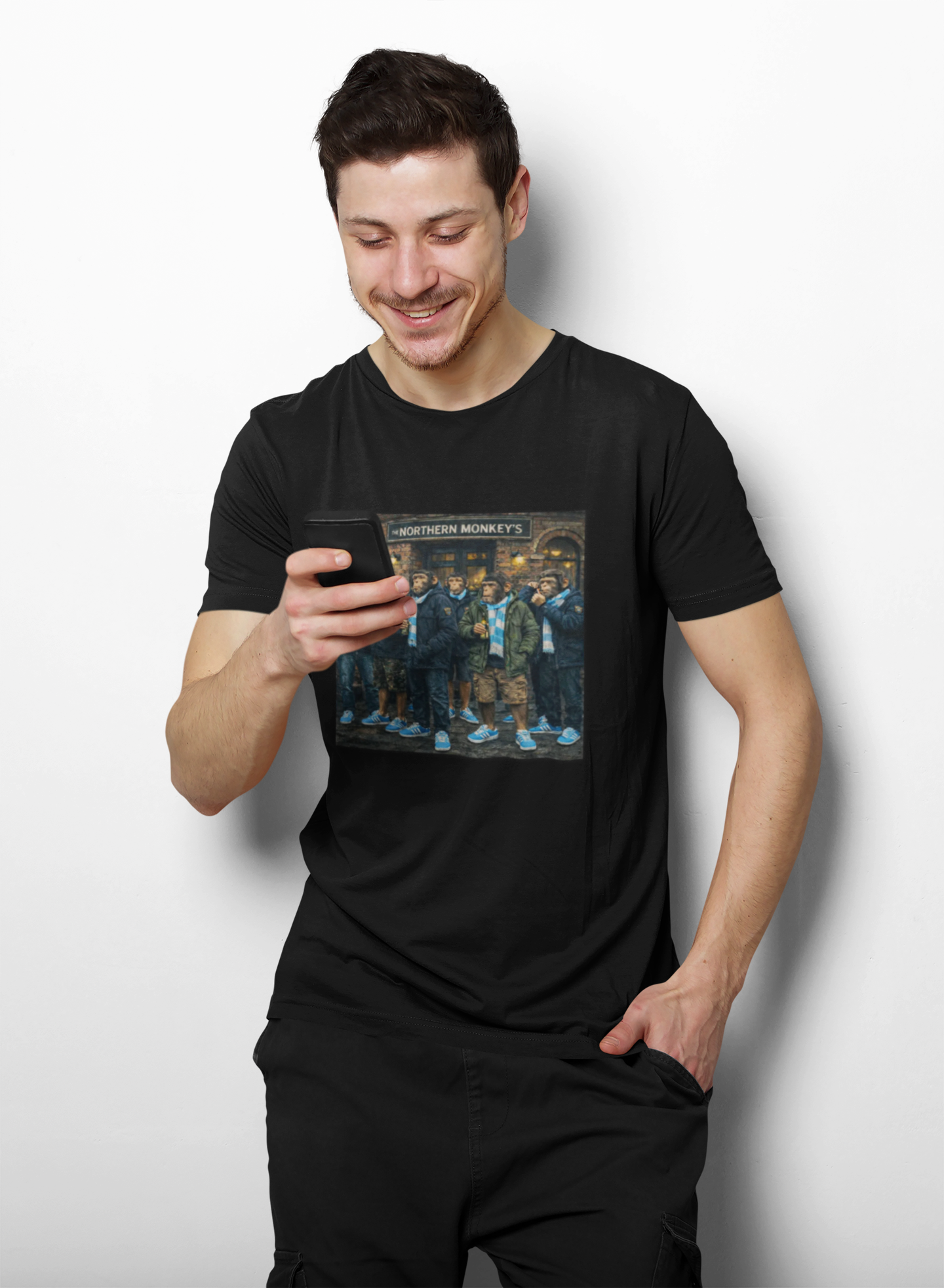 Man wearing a black Man City Northern Monkeys t-shirt with a graphic design, holding a phone.