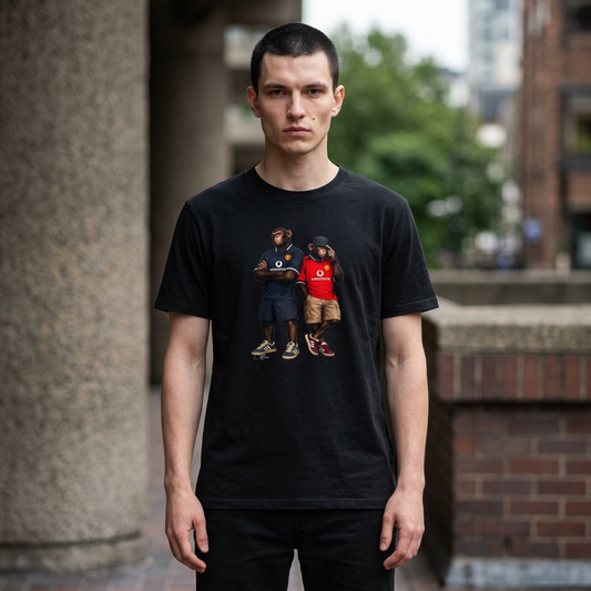 Person wearing a black short-sleeved t-shirt featuring a central graphic of two chimpanzees styled as Manchester United FC fans. The chimpanzee on the left stands with arms crossed, wearing the 2001-02 black away jersey with the white "vodafone" sponsor and white collar. The chimpanzee on the right wears the classic red Manchester United home kit from the same era in an urban setting