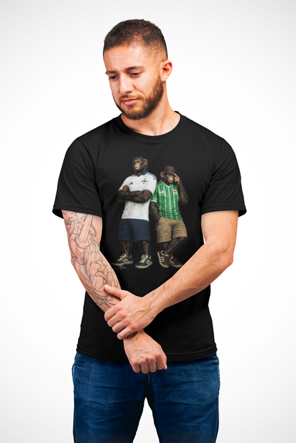 Man wearing a black short-sleeved t-shirt featuring a central graphic of two chimpanzees styled as Northern Ireland national team supporters. The chimpanzee on the left stands with arms crossed, wearing a white away jersey with blue trim and the Northern Ireland crest. The chimpanzee on the right wears the classic green home jersey with vertical stripes, khaki cargo shorts, and a maroon bucket hat on a white background