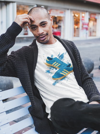 A man sitting on a white bench wearing a black waffle-knit cardigan over a white graphic t-shirt featuring a blue and yellow sneaker print, with a blurred street background.