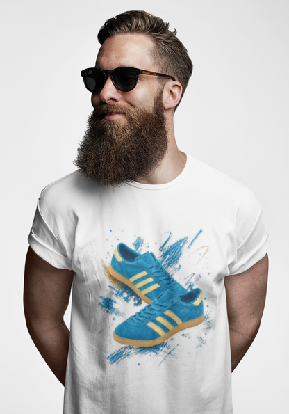 A man with a full beard and sunglasses wearing a white t-shirt with a graphic print of blue Adidas sneakers with yellow stripes, set against a plain light gray background.