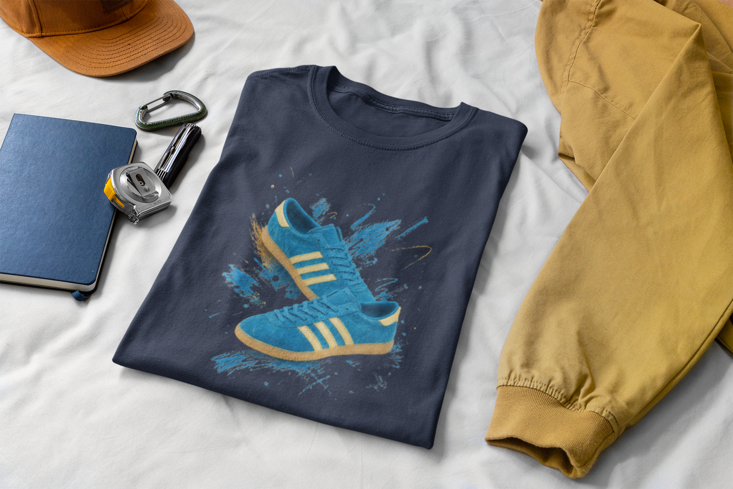 Navy blue t-shirt with a printed graphic of a blue suede trainer featuring cream stripes and a gum sole, surrounded by a blue and gold paint splatter design, with an "On The Terrace" logo on the neck label.