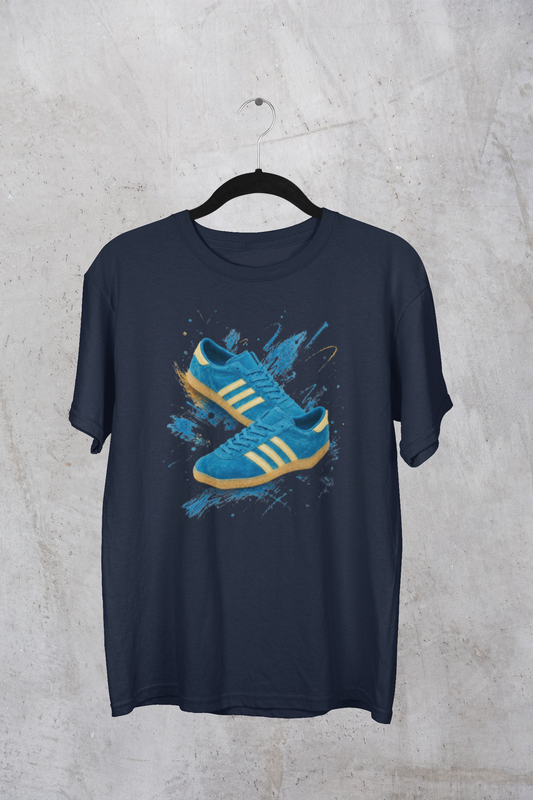 Navy blue t-shirt with a printed graphic of a blue suede trainer featuring cream stripes and a gum sole, surrounded by a blue and gold paint splatter design, with an "On The Terrace" logo on the neck label.
