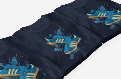 A close-up of folded navy blue t-shirts arranged diagonally, each featuring a graphic print of blue sneakers with yellow stripes and splatter-style artwork.