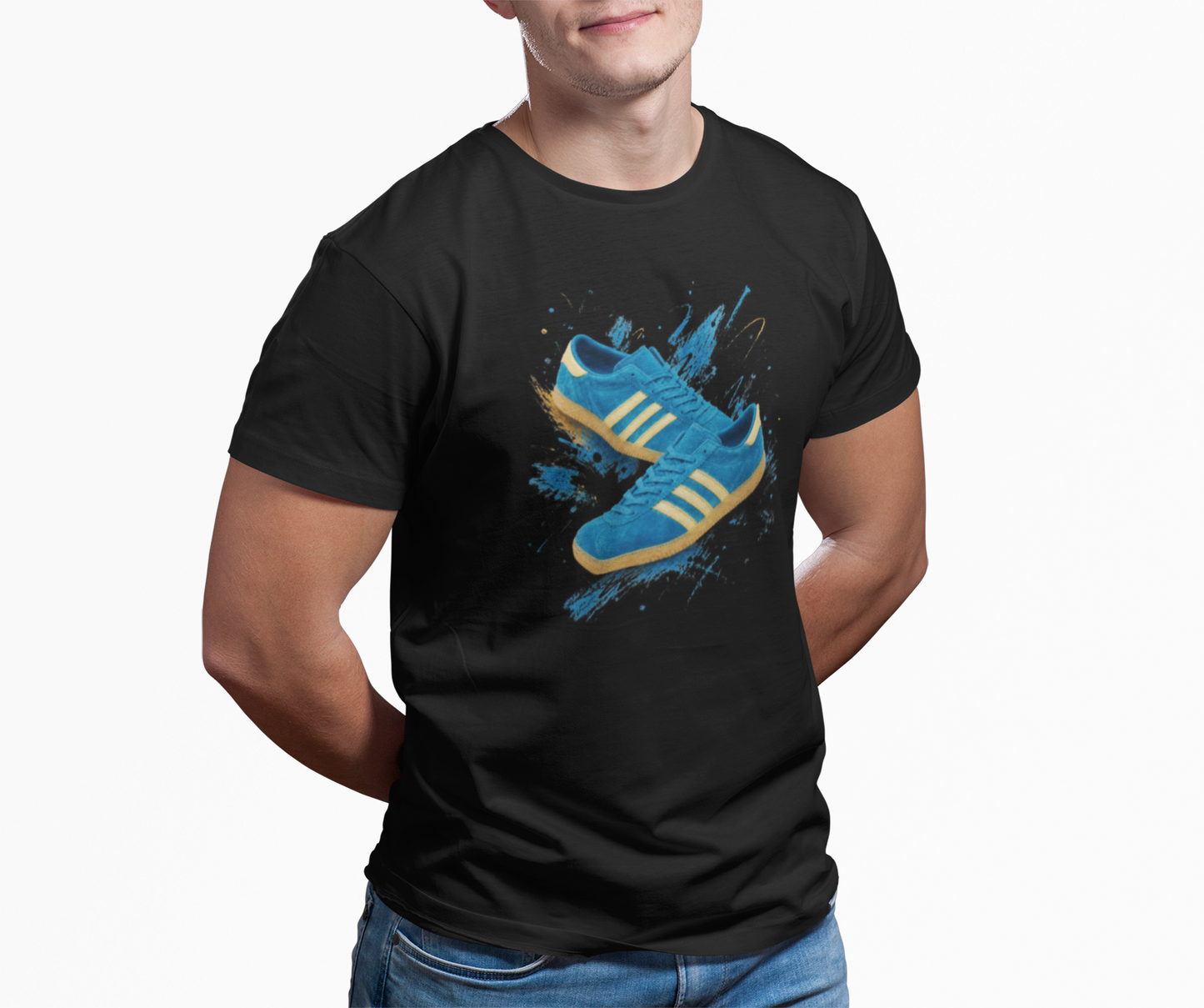 A man wearing a black short-sleeve t-shirt with a graphic print of blue sneakers with yellow stripes on a splattered blue background, paired with blue jeans against a plain white studio background.