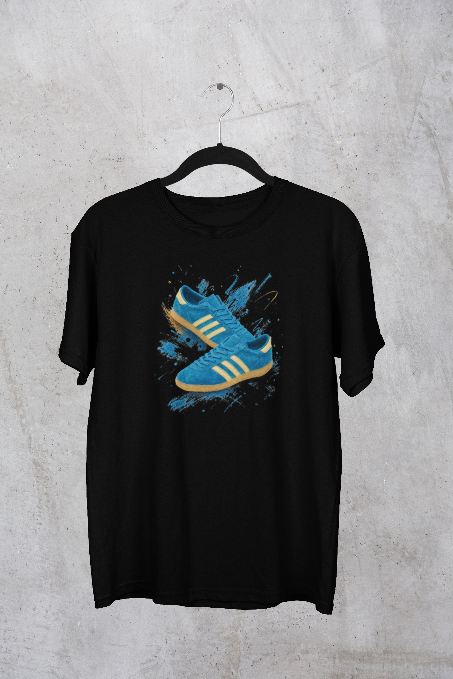 A black short-sleeve t-shirt hanging on a black hanger against a textured gray concrete wall. The shirt features a graphic print of a blue and yellow sneaker with blue paint splatters on the front.