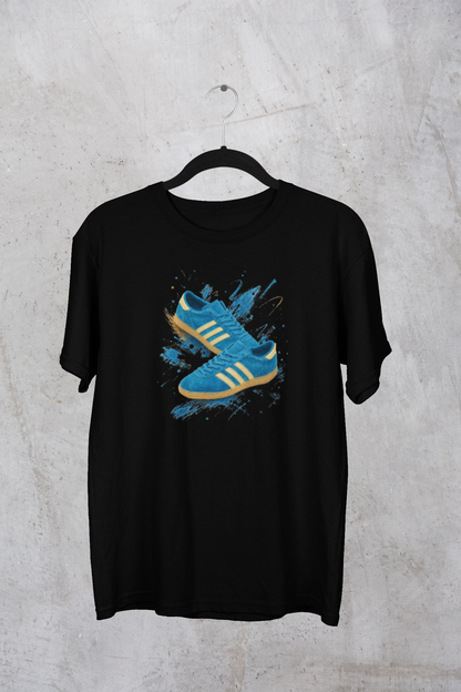 A black short-sleeve t-shirt hanging on a black hanger against a textured gray concrete wall. The shirt features a graphic print of a blue and yellow sneaker with blue paint splatters on the front.