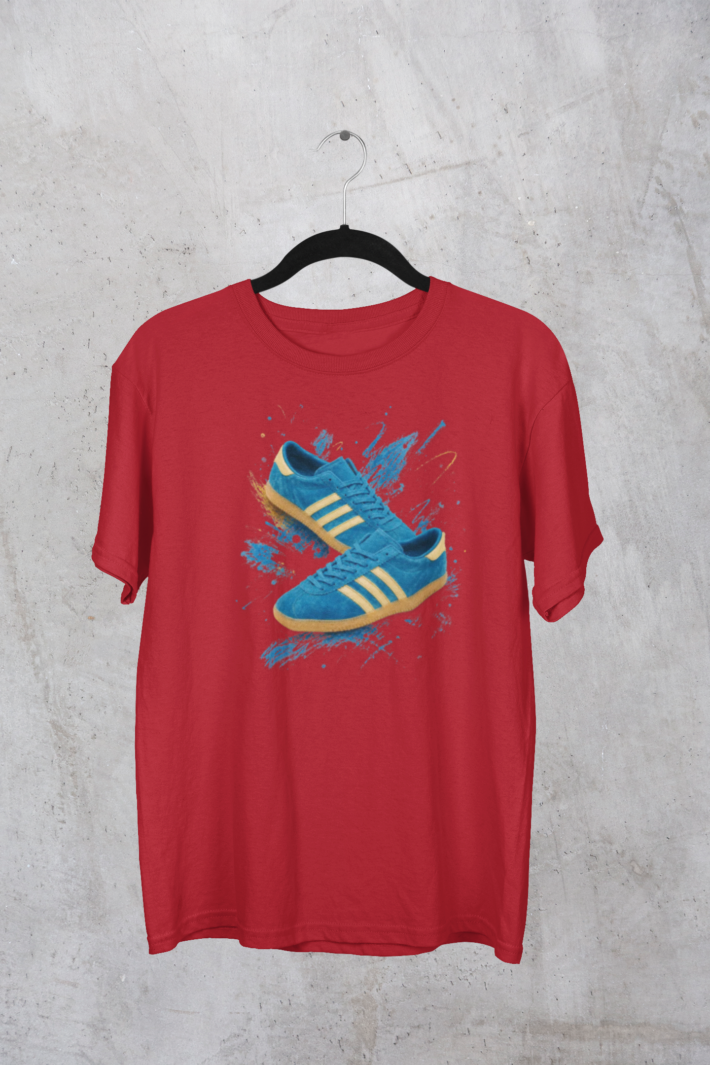 A red short-sleeve t-shirt hanging on a black hanger against a textured gray concrete wall. The shirt features a graphic print of blue sneakers with yellow stripes and blue paint splatters on the front.