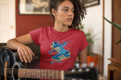 A woman with curly hair wearing a red graphic t-shirt with a blue and yellow sneaker print, holding an acoustic guitar in a warm, indoor room setting.