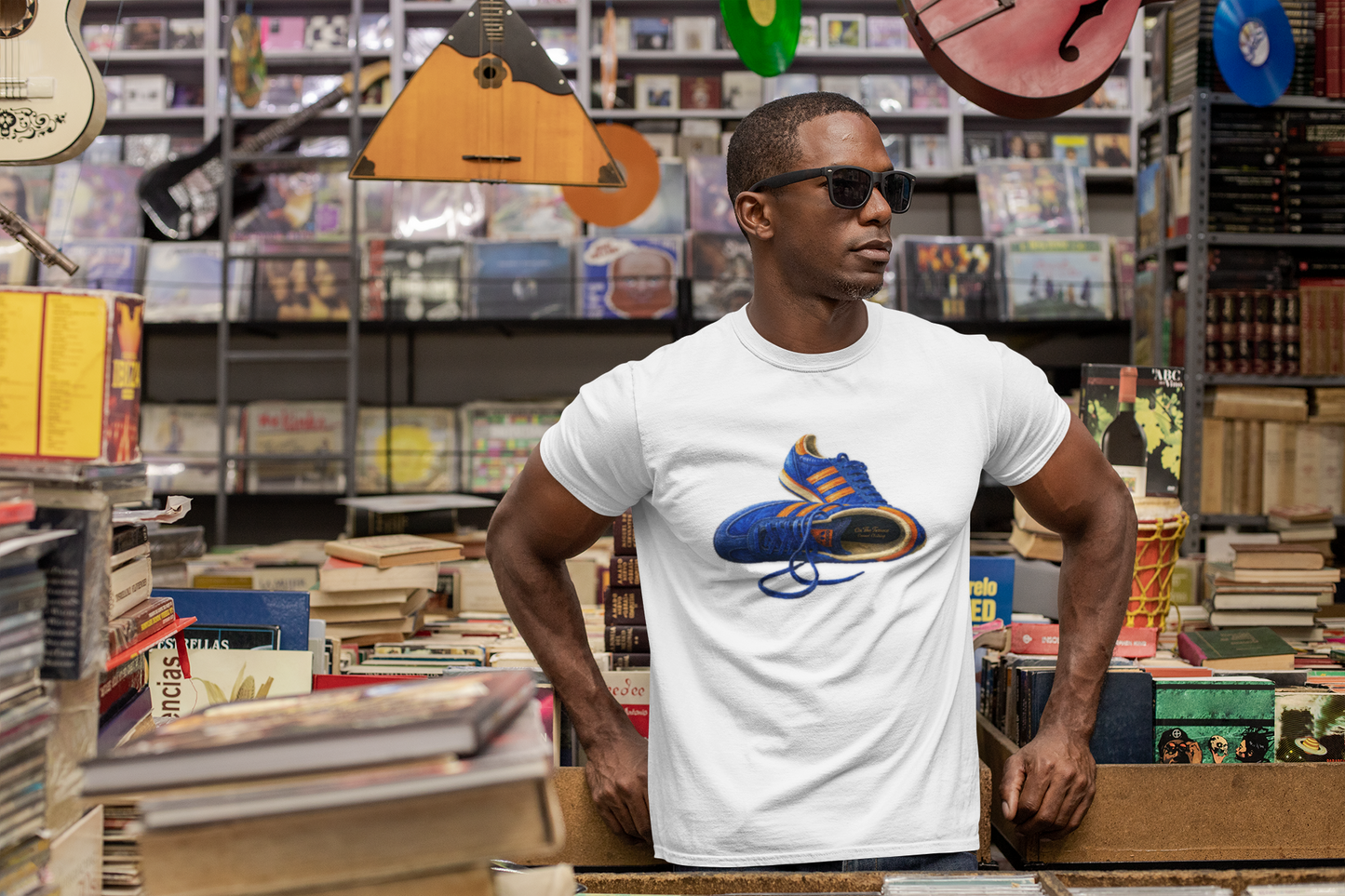 A man wearing a white t-shirt with illustration of blue and orange adidas Gazelle-style trainers, terrace casual sneaker graphic tee, vintage trainer collection, On The Terrace