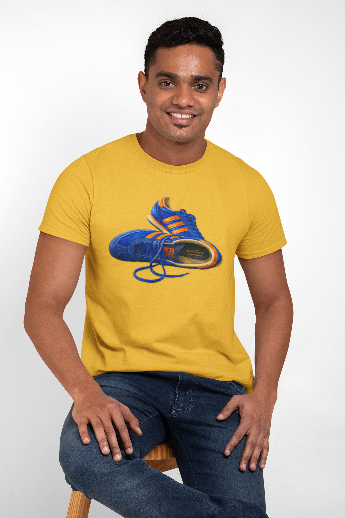 A man wearing a Gold t-shirt with hand-illustrated blue and orange retro terrace trainer sneaker graphic print, On The Terrace casual clothing brand
