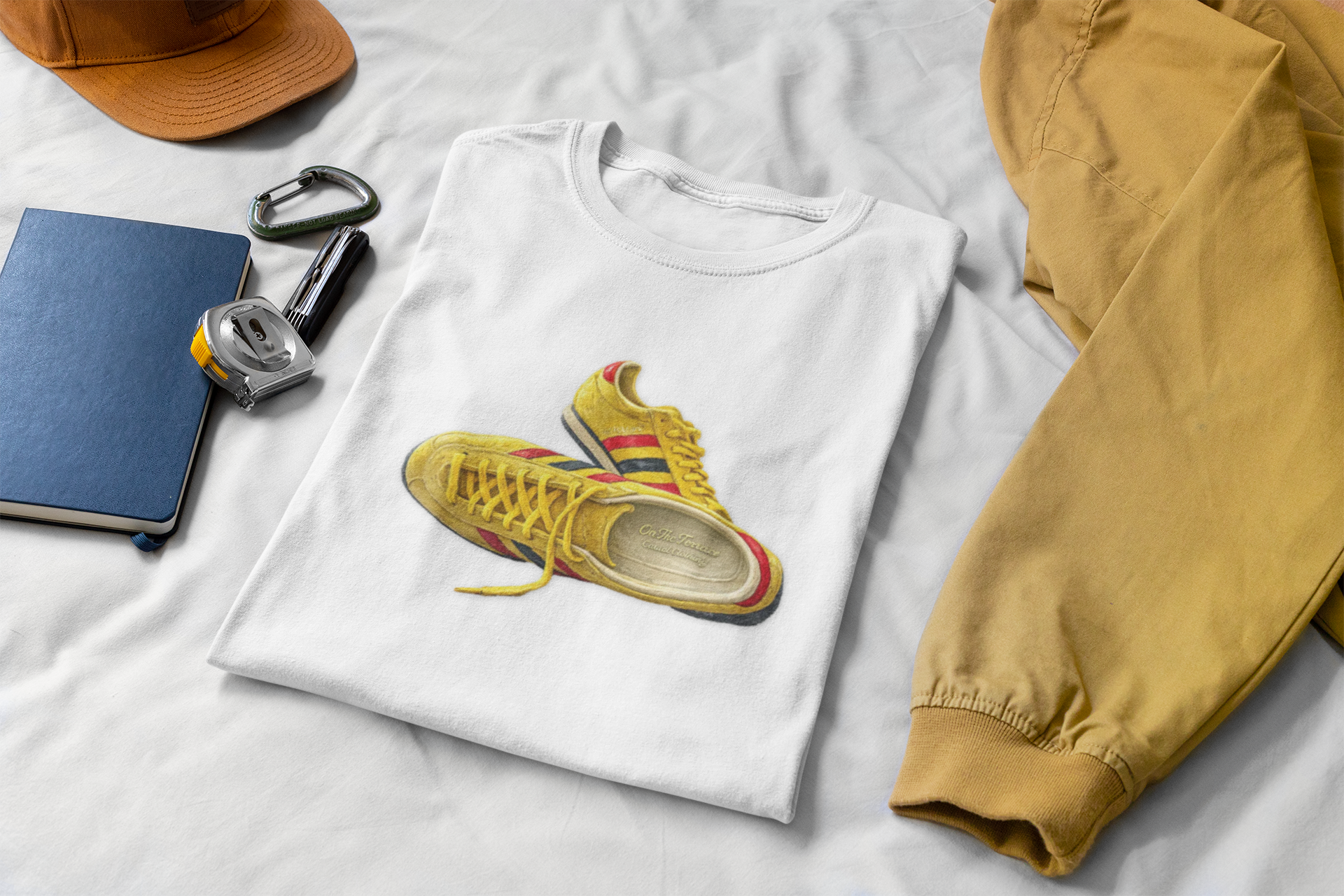 A folded white t-shirt with hand-illustrated yellow, navy and red retro terrace trainer sneaker graphic print, On The Terrace casual clothing brand

