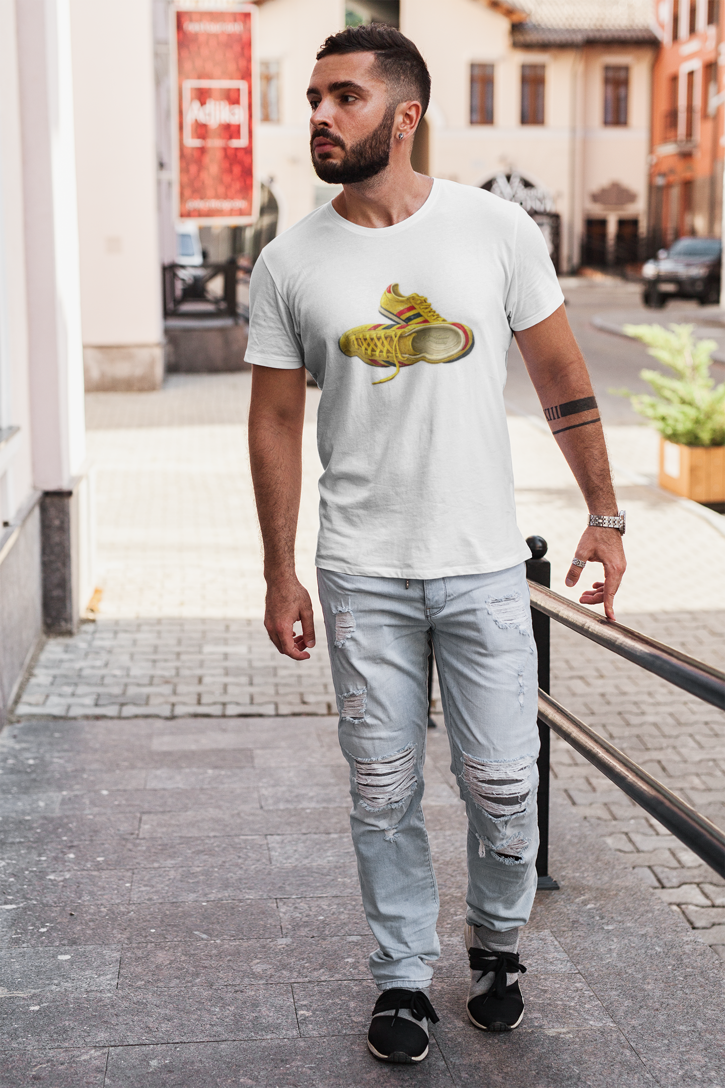 A man walking outdoors on a city street wearing a white crew-neck t-shirt with hand-illustrated yellow, navy and red retro terrace trainer sneaker graphic print, On The Terrace casual clothing brand
