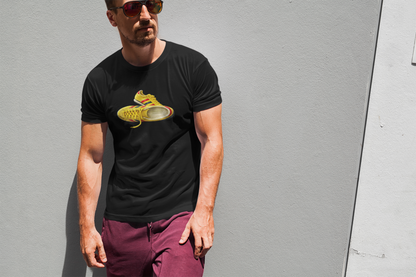 A man wearing a black crewneck t-shirt with hand-illustrated yellow, navy and red retro terrace trainer sneaker graphic print, On The Terrace casual clothing brand, paired with maroon pants, standing against a gray wall.