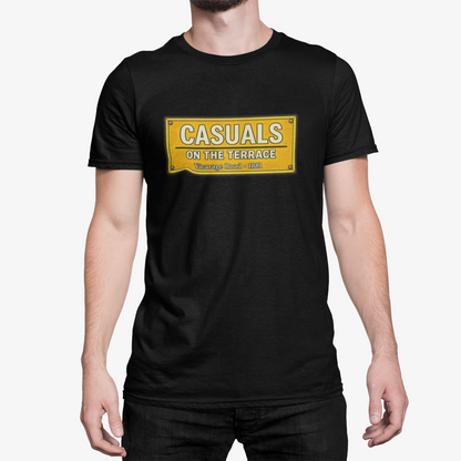 A man wearing a black short-sleeve Watford t-shirt with a yellow rectangular graphic on the chest that reads 'CASUALS ON THE TERRACE'.