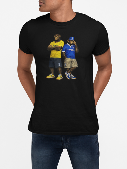 A man wearing a black short-sleeve Birmingham t-shirt with a graphic print of two football players in yellow and blue jerseys, paired with blue jeans, against a light gray background.