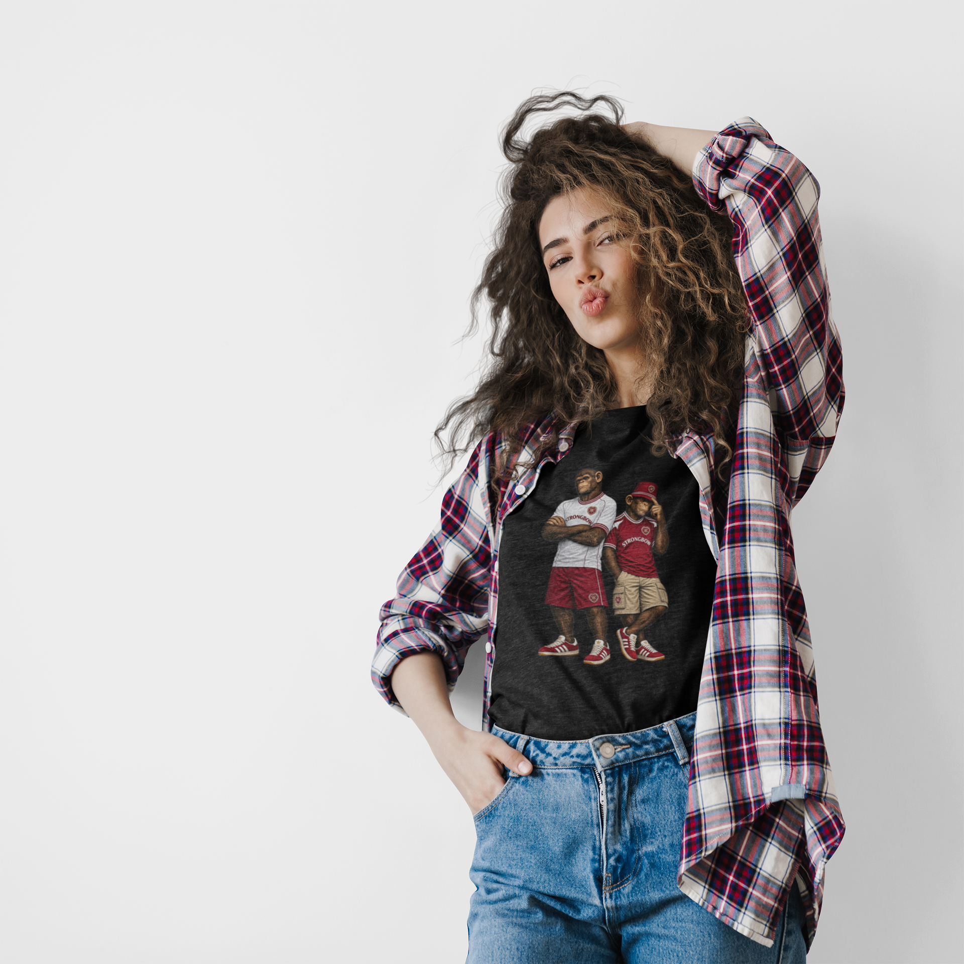 A model wearing a black graphic Hearts t-shirt with a vintage-style basketball player print, styled with an open red and white plaid flannel shirt and blue jeans against a plain white background.