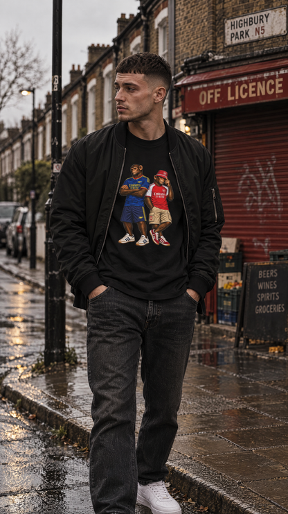 A man stands on a wet cobblestone street wearing a black bomber jacket over a Arsenal Emirates Era Duo t-shirt in black styled with denim - On The Terrace casual wear