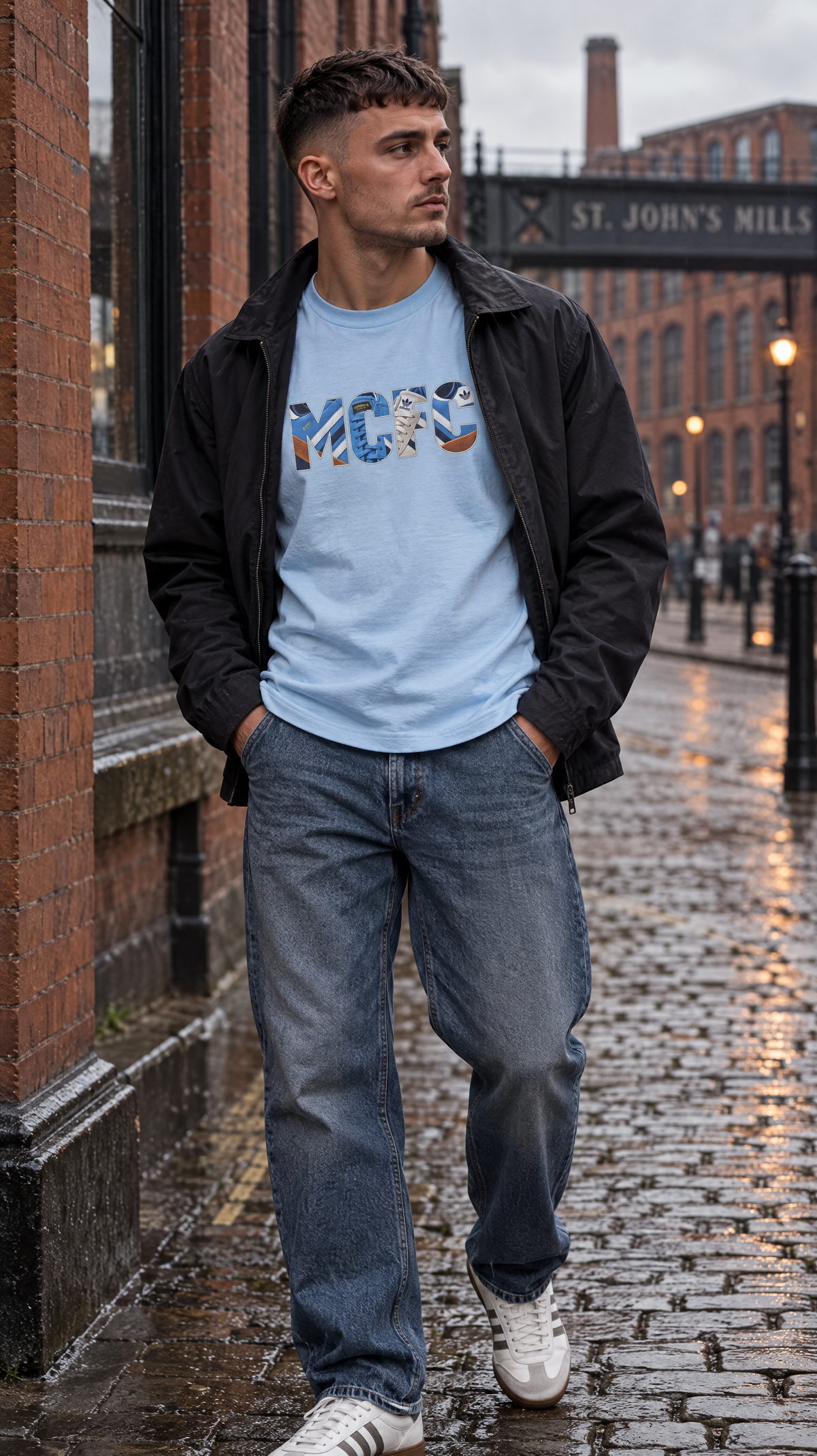 A man standing on a wet cobblestone street wearing a Manchester City-inspired light blue terrace tee with retro trainer artwork